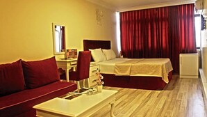 Quarto de hotel com cama, escrivaninha, cadeira, mesinha e cortina vermelha.