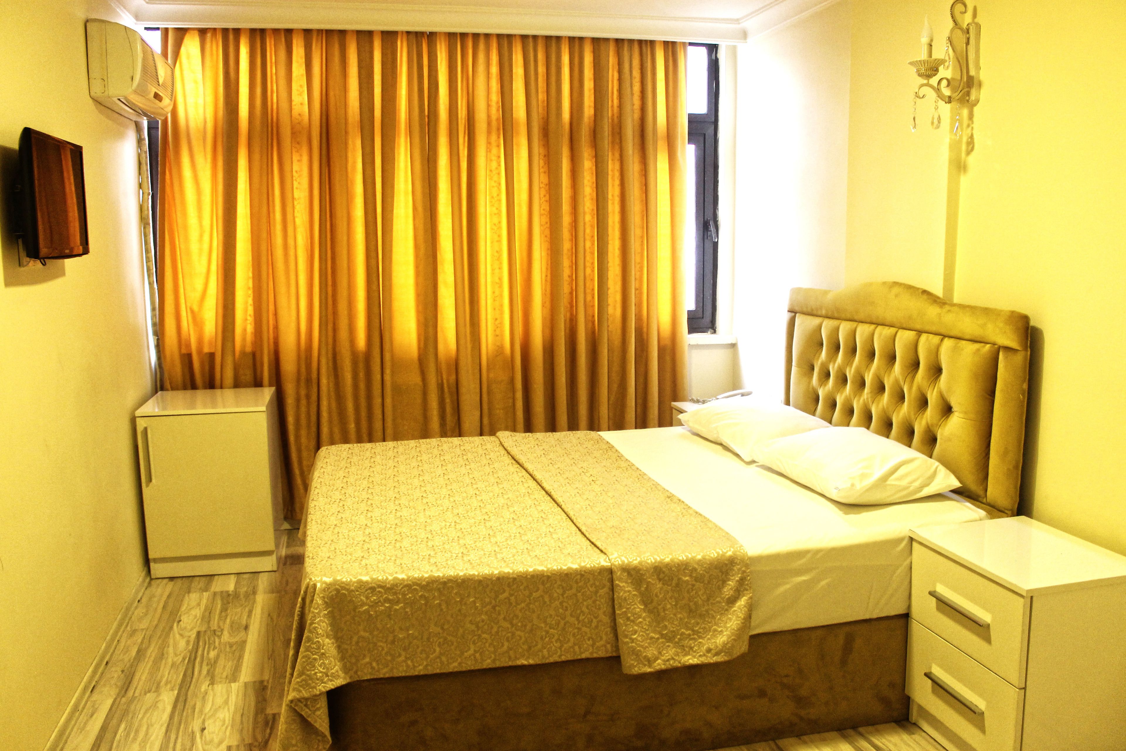 A hotel room with a bed, bedside table, nightstand, and an air conditioning unit.