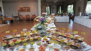 Een buffet met diverse gerechten en dranken, omringd door stoelen en tafels in een ruime zaal.