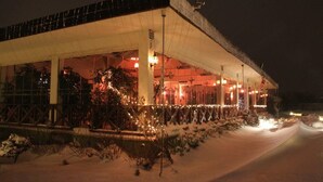 Een gebouw met een overdekt buitengebied, mogelijk een restaurant of café, met een met sneeuw bedekte grond en verlichting.