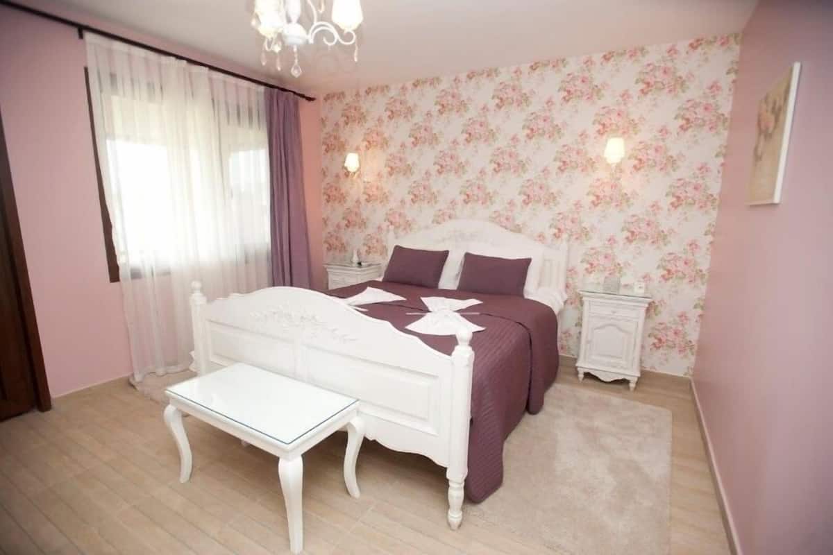 Un dormitorio con una cama blanca, una mesita pequeña, una mesita de noche y un papel tapiz floral.