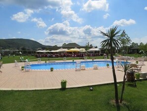 A pool area with lounge chairs and umbrellas, surrounded by a grassy lawn and a building in the background. - Riva's Club (Çekmeköy)