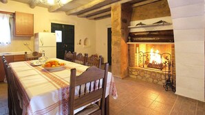 A dining area with a fireplace, wooden ceiling beams, and a table set with fruits. - Villa Laina (Platanias)