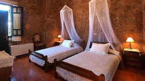 A rustic room with two beds, each with a canopy, a wooden chair, a small table, and a wall-mounted lamp. - Villa Laina (Platanias)