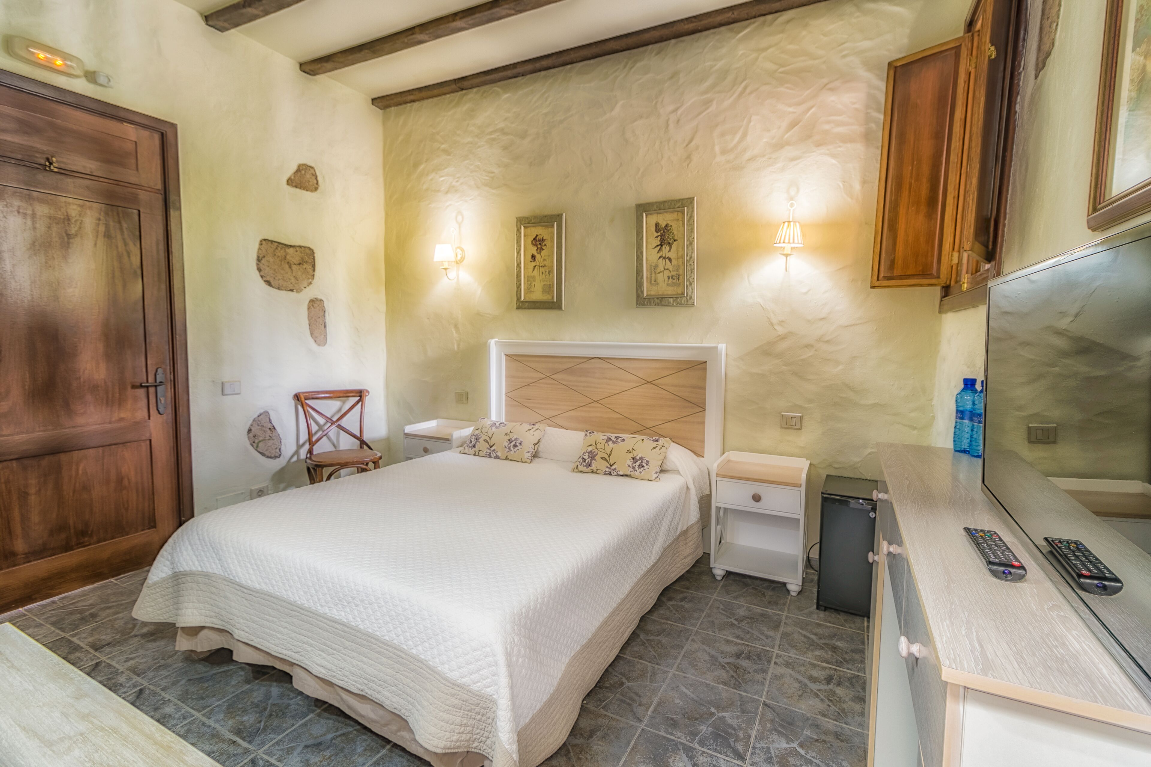A bedroom with a large bed, bedside tables, a dresser, a mirror, and a TV.
