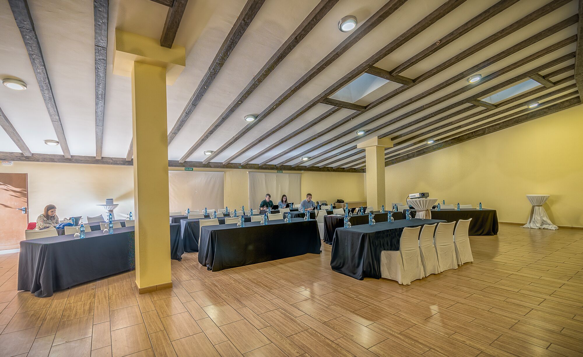 Een congreszaal met lange tafels, stoelen en een houten plafond.