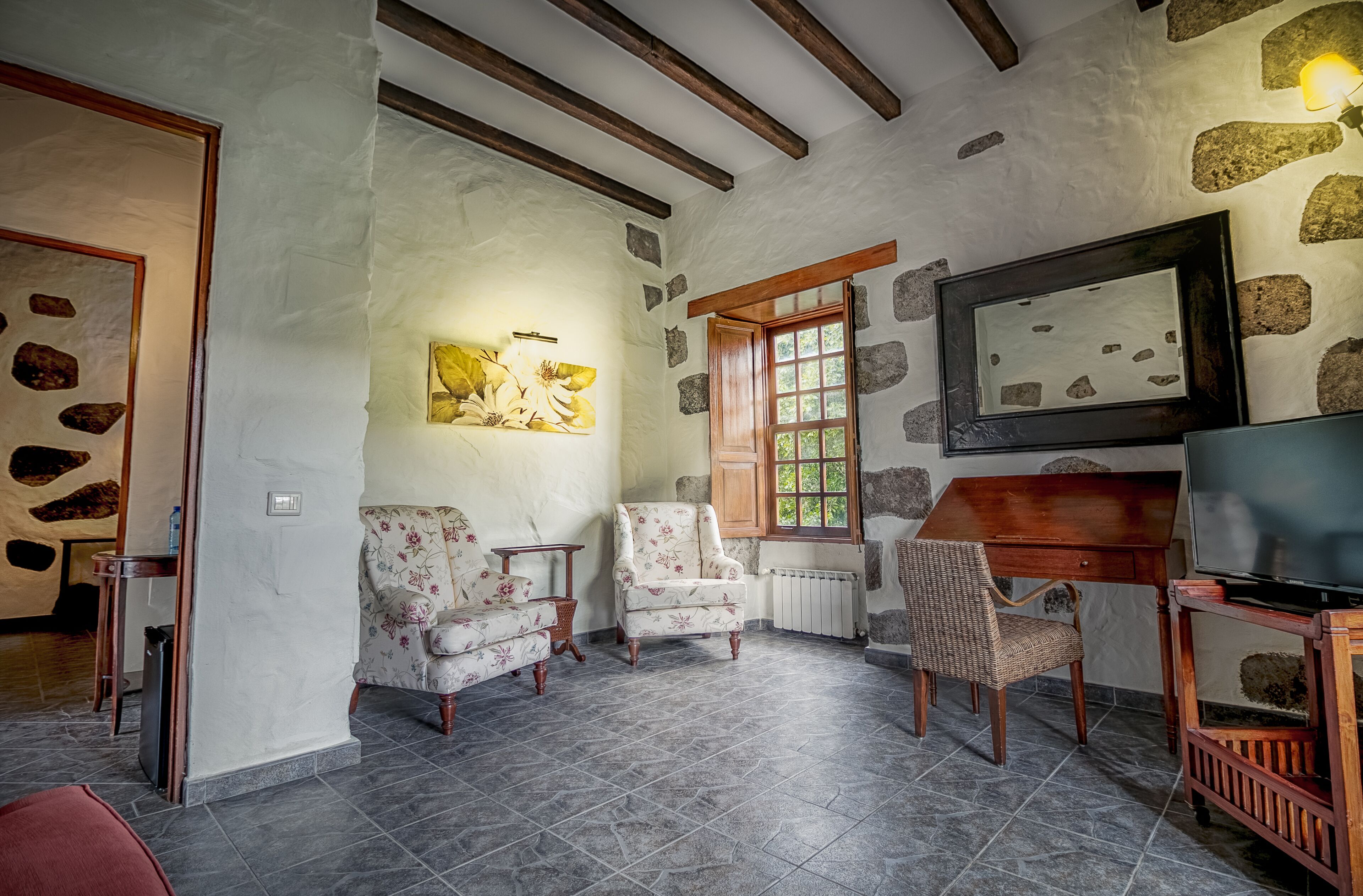 Una sala de estar acogedora con paredes de piedra, vigas de madera y chimenea. Hay dos sillones, un televisor y una mesa.