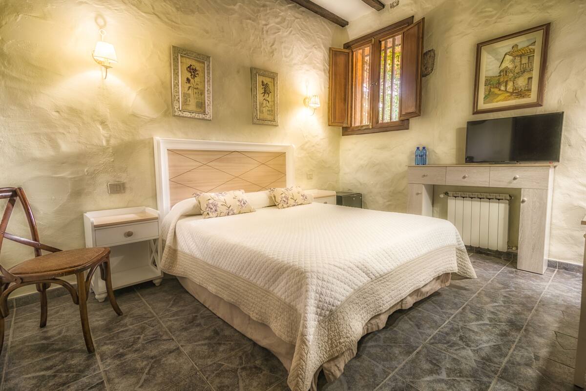 A bedroom with a bed, nightstand, chair, dresser, television, and wall-mounted lamps.