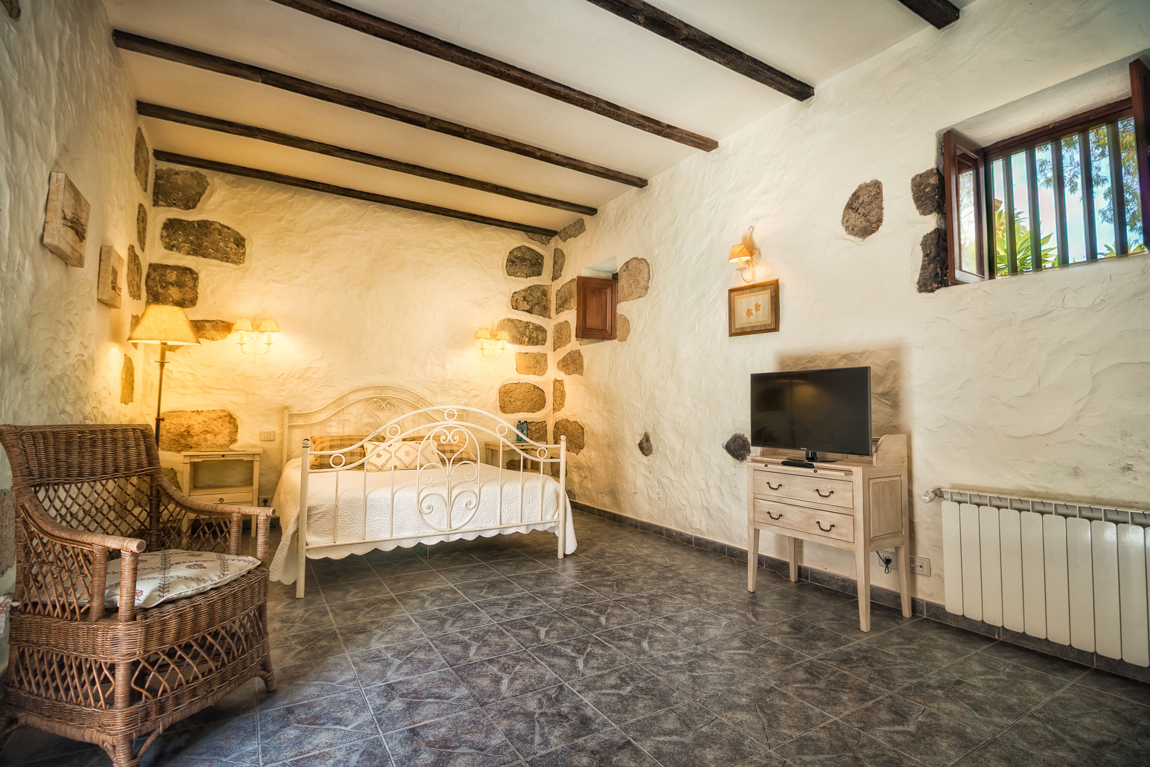 Een slaapkamer met een stenen muur, een bed, een stoel, een televisie en een dressoir.