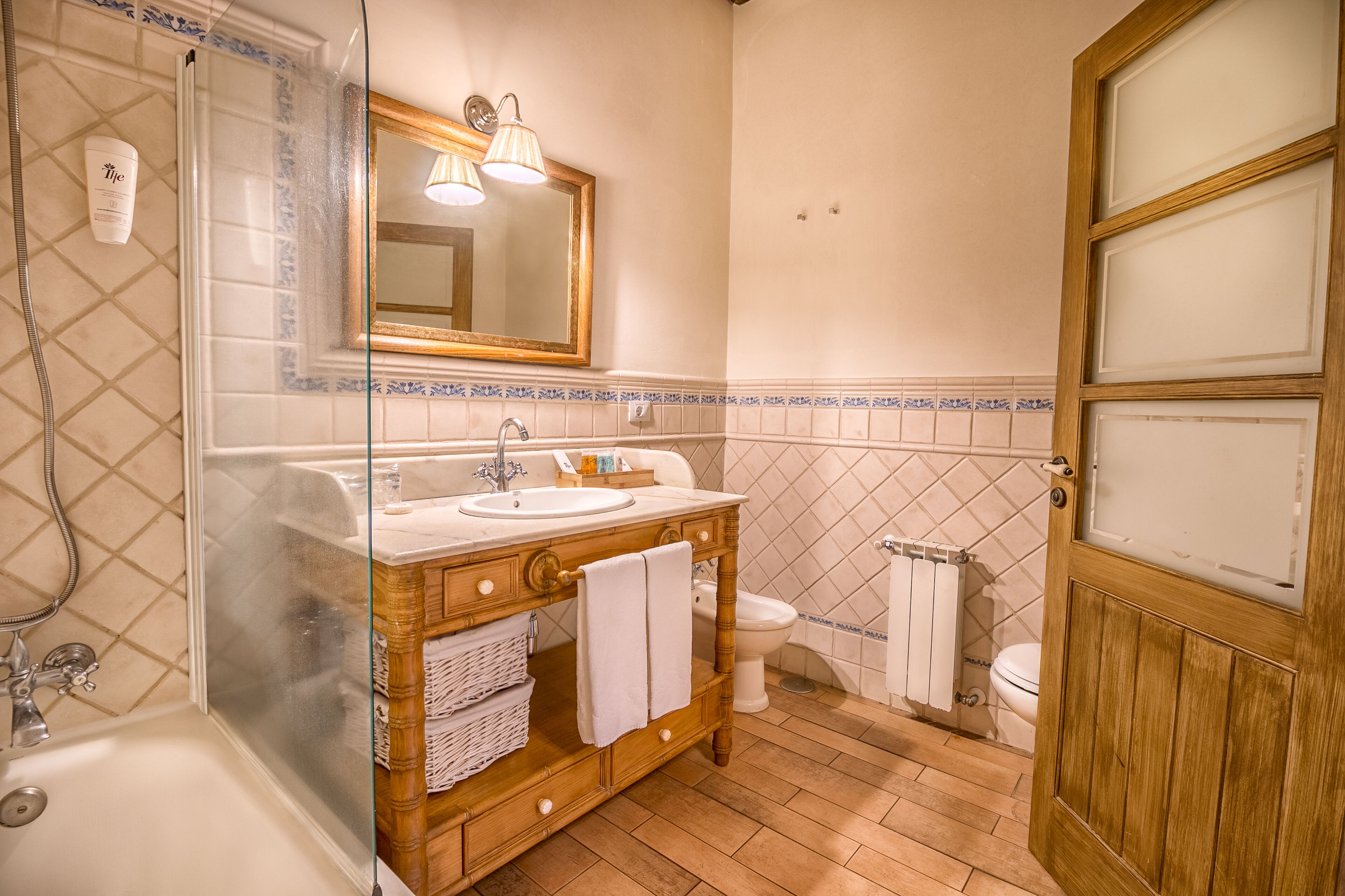 A bathroom with a glass-enclosed shower, a wooden vanity with a sink and mirror, and a toilet with a radiator.