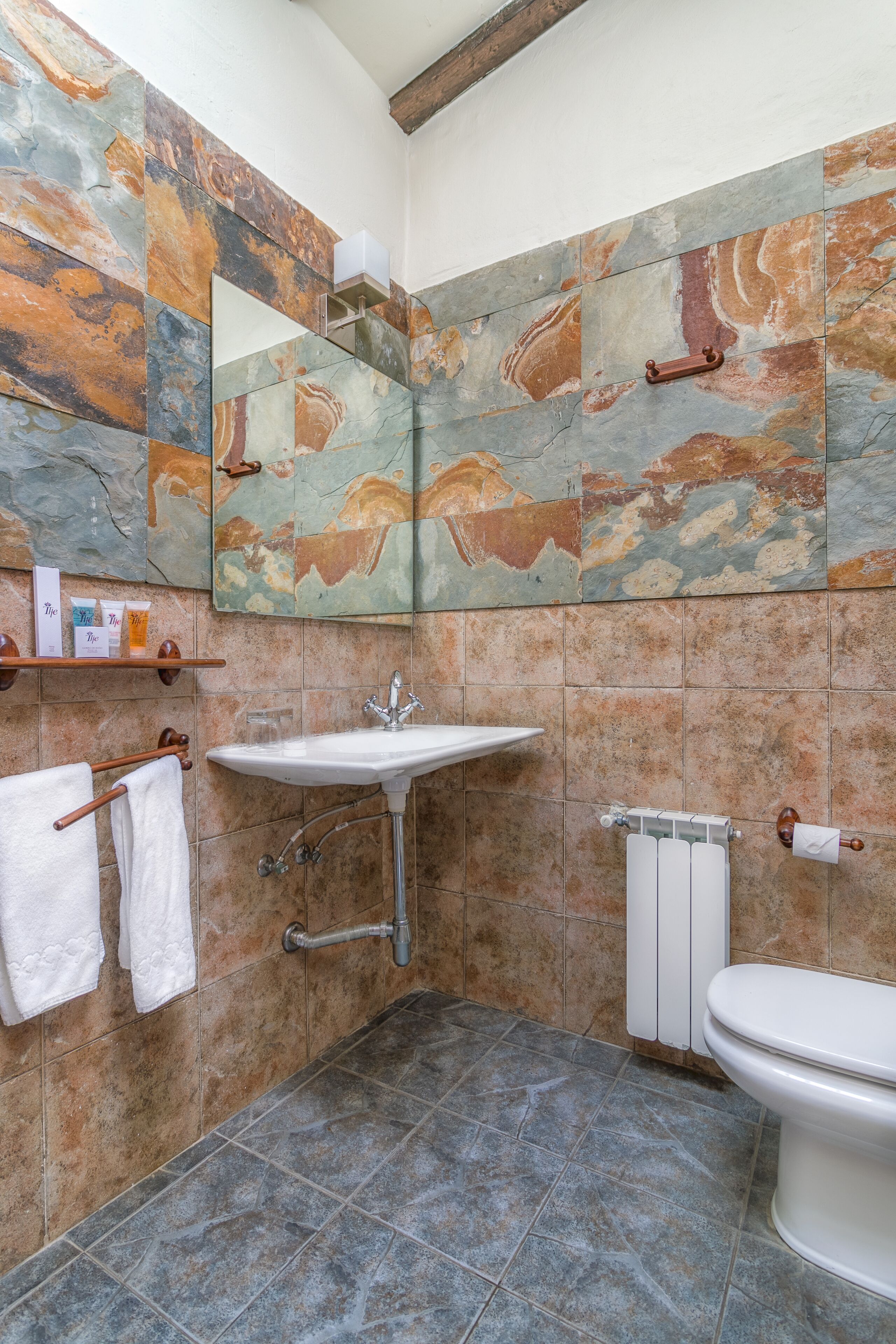 Un baño con suelo de baldosas de piedra, un lavabo blanco, un inodoro y un espejo sobre el lavabo.