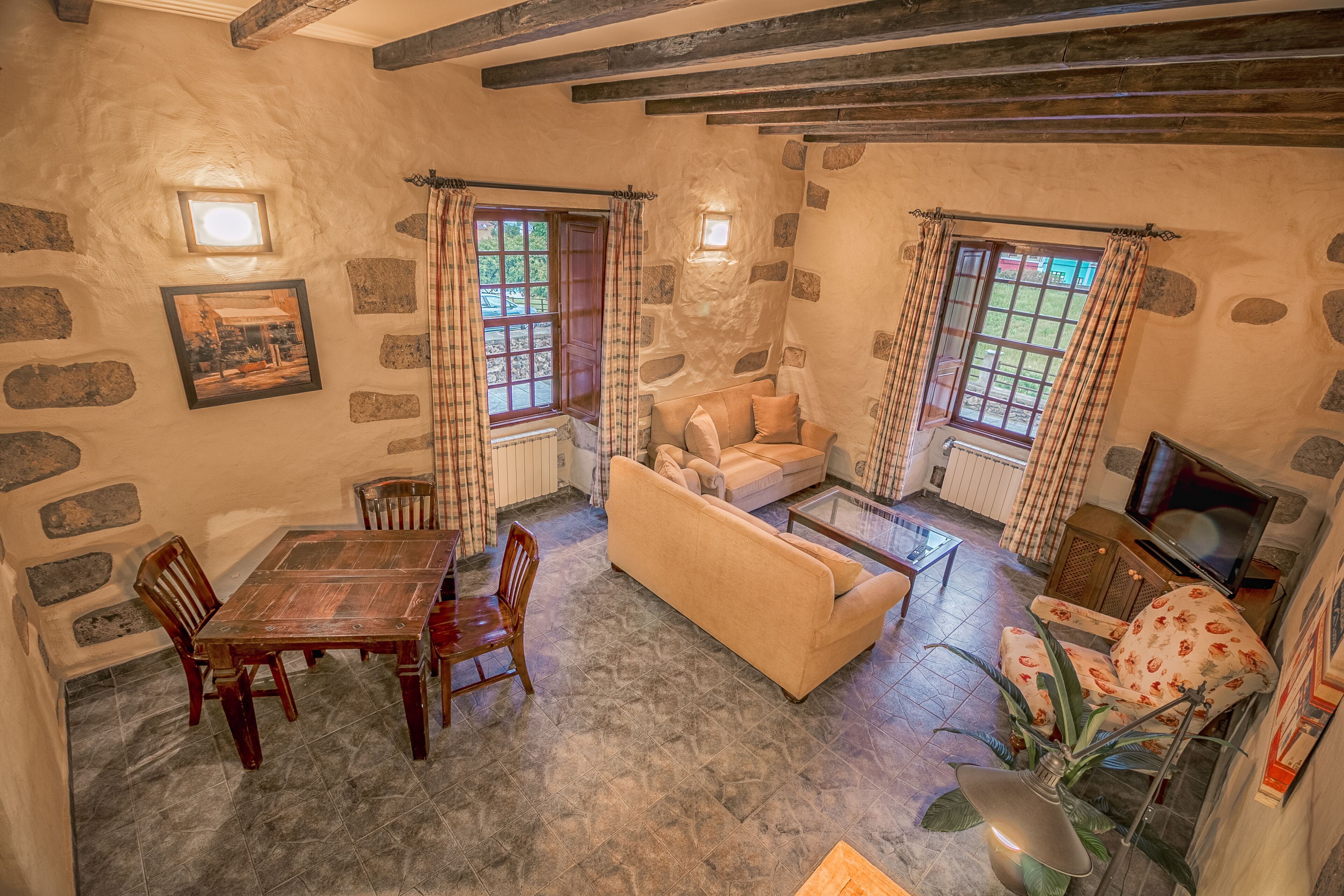 Una sala de estar acogedora con una pared de piedra, una mesa de comedor de madera, un sofá y un televisor.