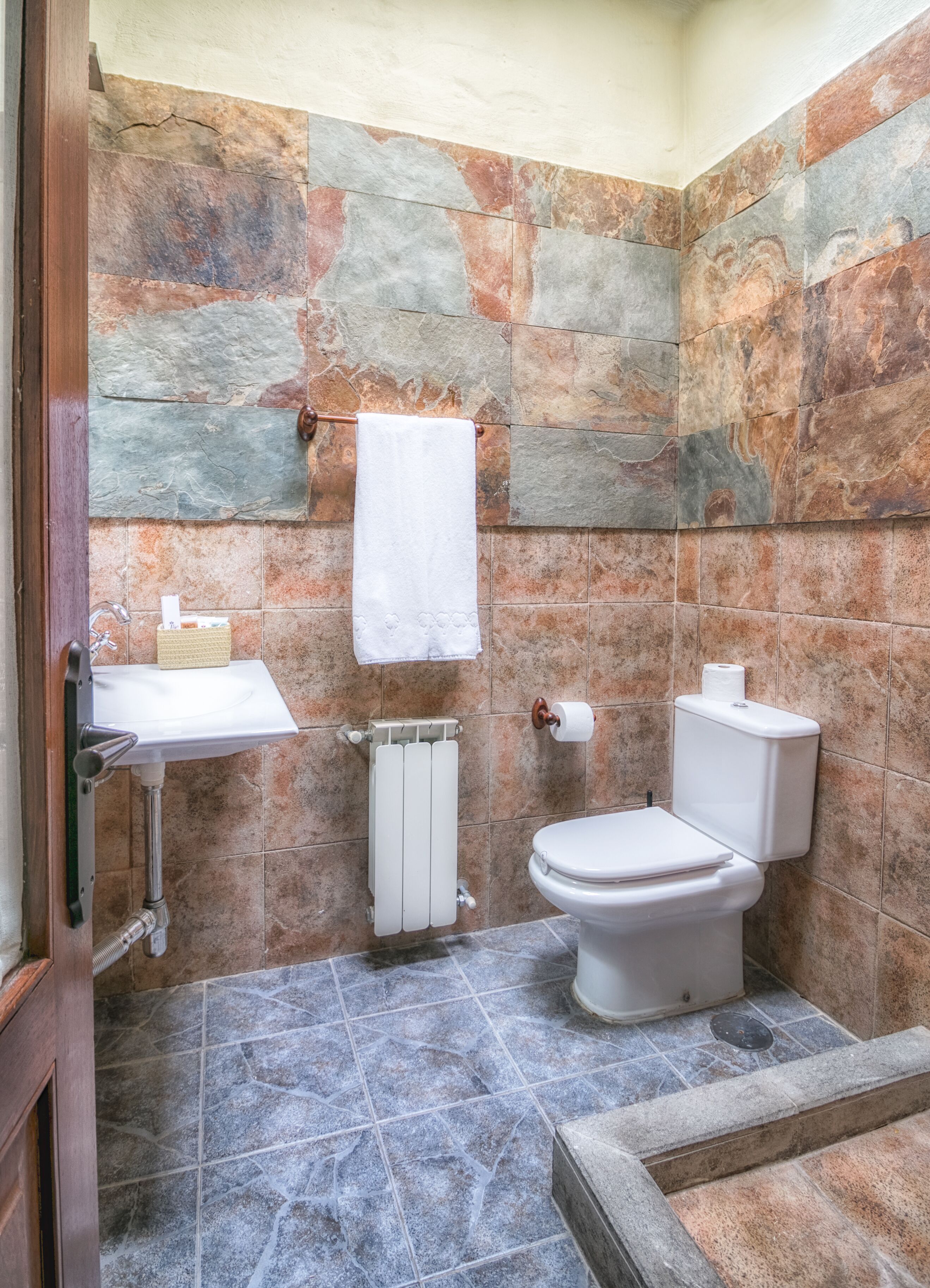 Ein Badezimmer mit Steinwand, Waschbecken in Weiß, Toilette und Handtuch an einem Halter.