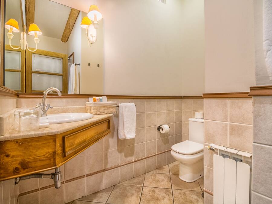 Un baño con tocador de madera, lavamanos, espejo, inodoro y toallero.