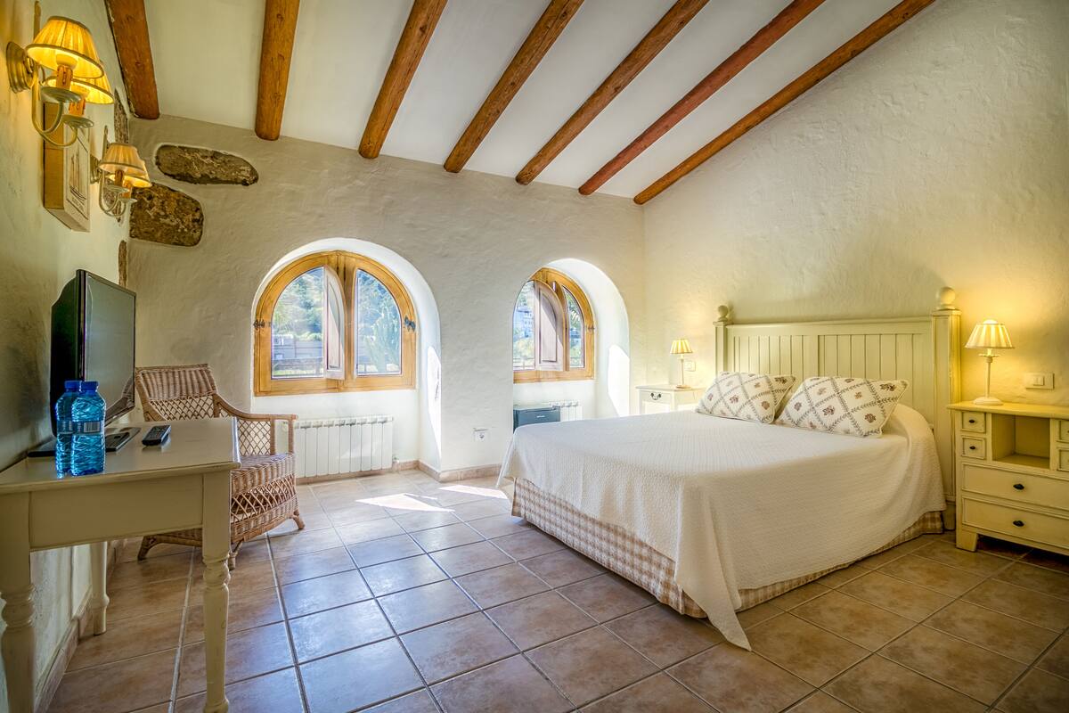 A bedroom with a bed, two windows, a desk, a chair, and a nightstand.