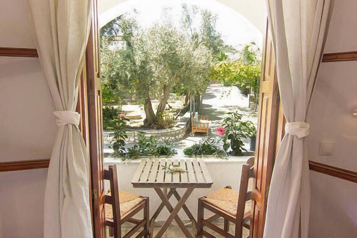 Un balcon avec une table en bois et deux chaises, donnant sur un jardin agrĂ©mentĂ© dâarbres et de plantes.