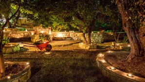 A well-lit garden area with stone walls, potted plants, and a wheelbarrow. - Naftilos Skiathos (Skiathos)