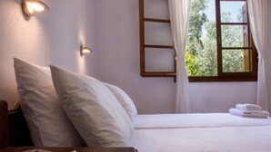 A neatly made bed with white linens, a bedside table with a magazine, and a window with curtains. - Naftilos Skiathos (Skiathos)