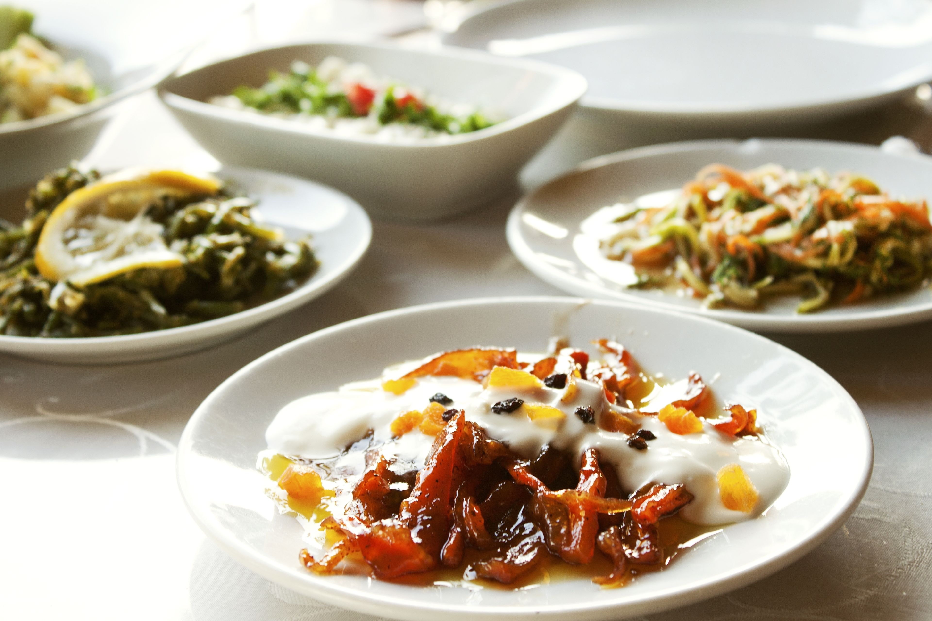 A table with various dishes, including a plate with a white sauce and vegetables, a bowl of salad, and another dish with greens and lemon slices.