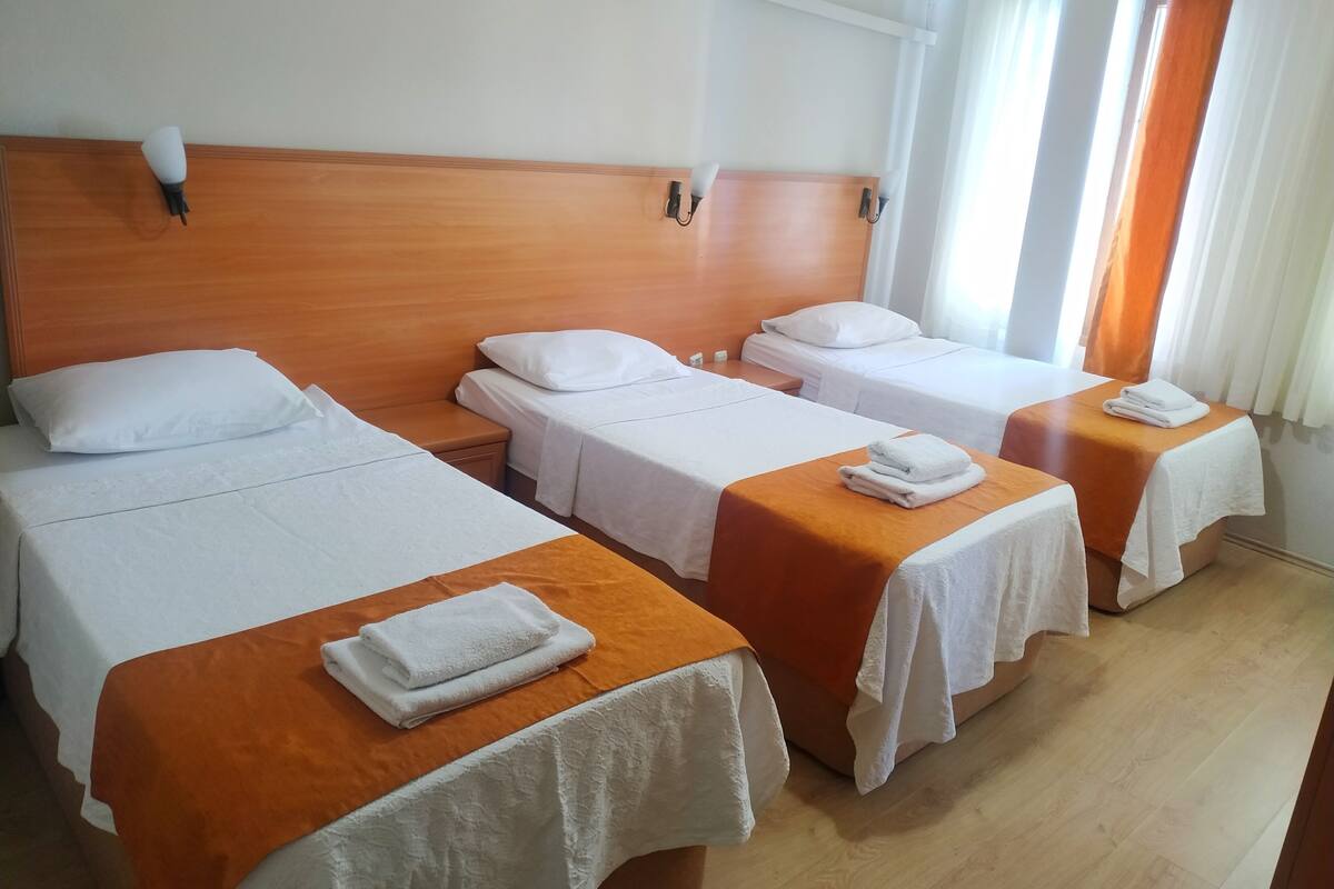 A hotel room with three single beds, each with a white bedspread and a folded towel on the side.