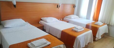 A hotel room with three single beds, each with a white bedspread and a folded towel on the side.