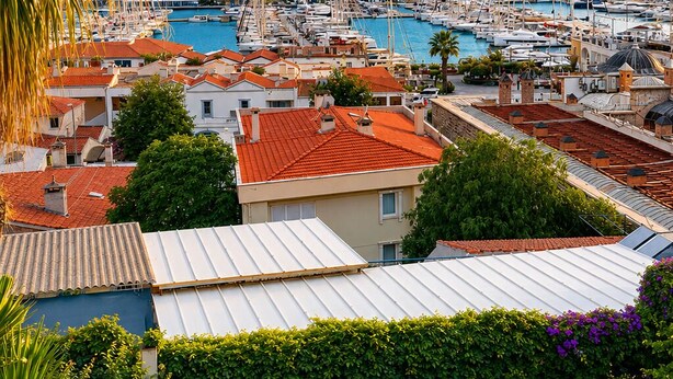 Un puerto deportivo con barcos, una colina al fondo y edificios residenciales con tejados rojos.