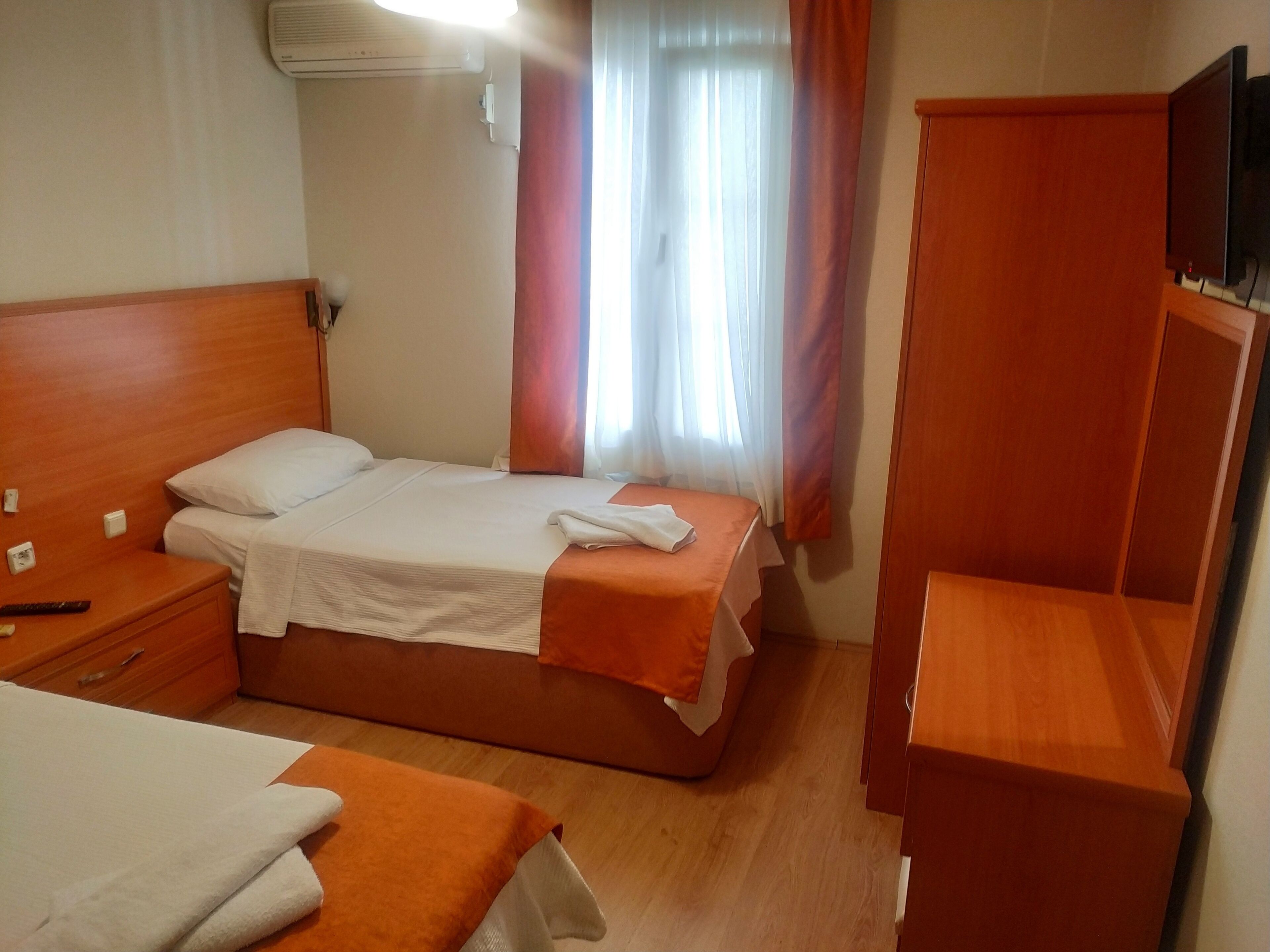 Habitación de hotel con una cama individual, una mesita de noche, un armario y un televisor.