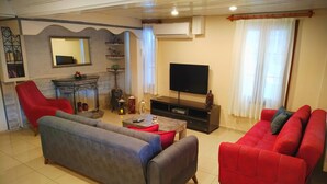 Un salón con un sofá gris, un sofá rojo, un sillón rojo, un televisor, una chimenea y una estantería.