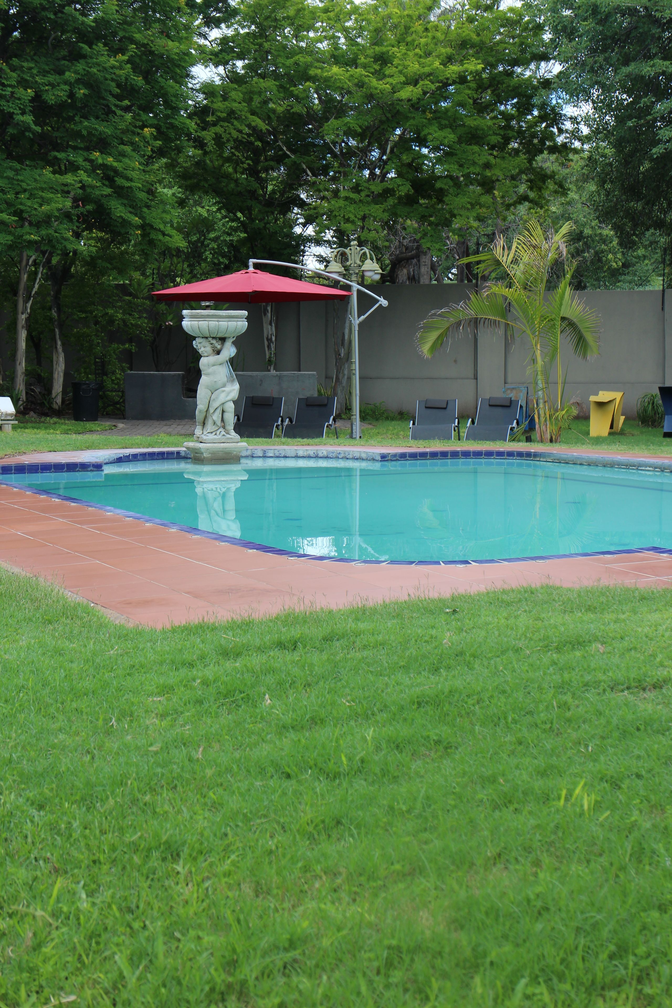 A swimming pool with a statue, a red umbrella, and lounge chairs.