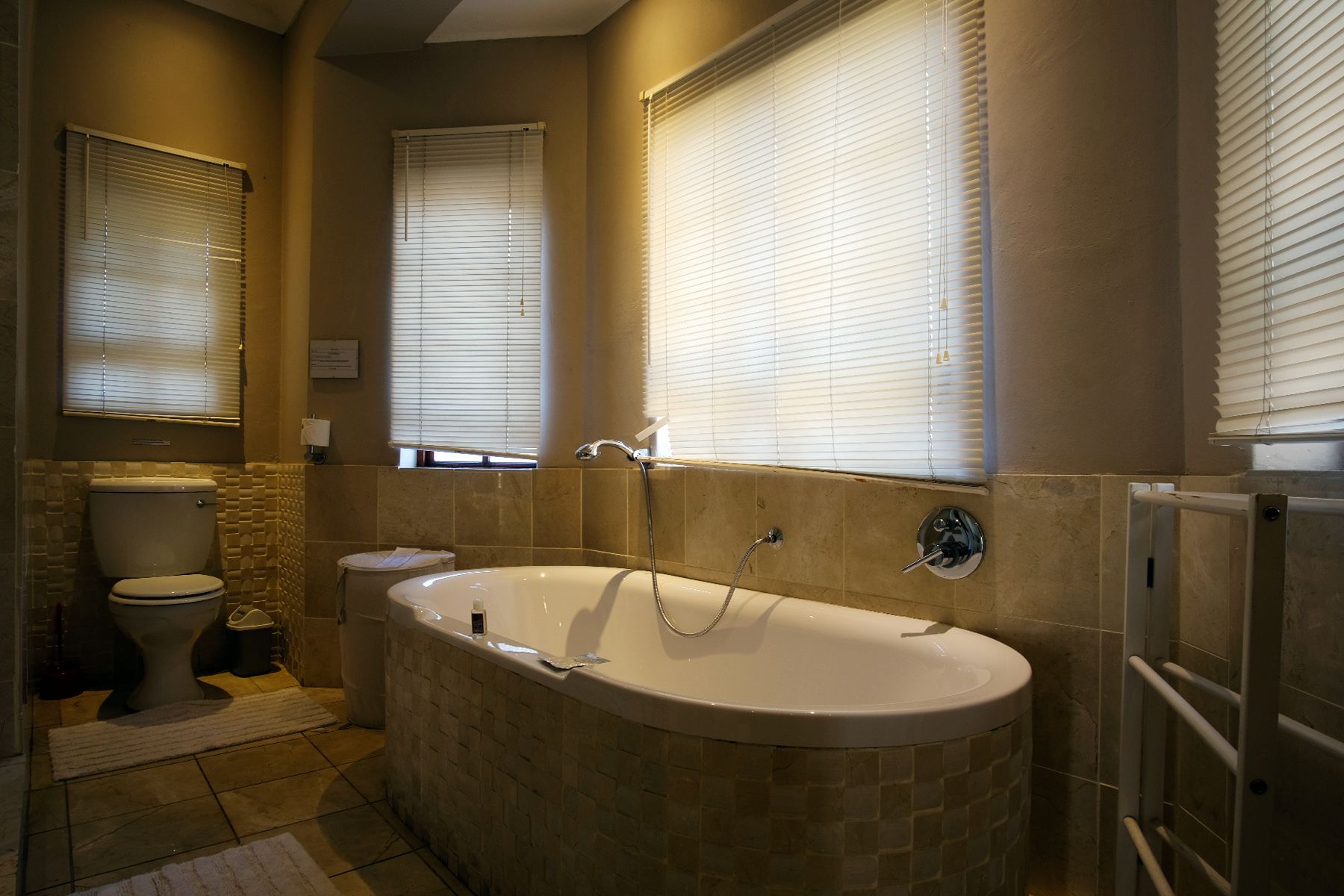 A bathroom with a freestanding bathtub, two toilets, and a window with blinds.
