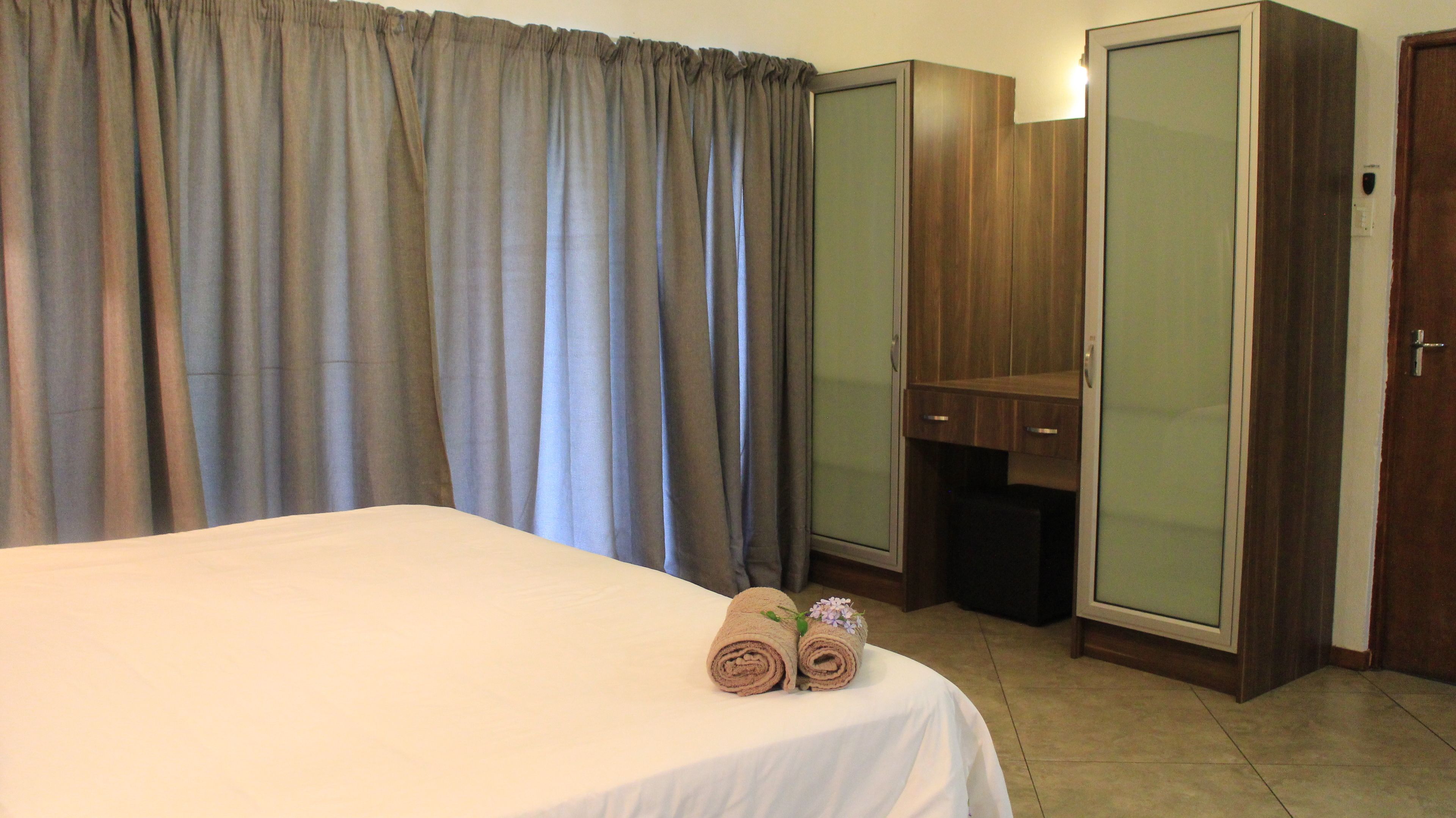 A hotel room with a bed, a wardrobe, a mirror, and a curtain.