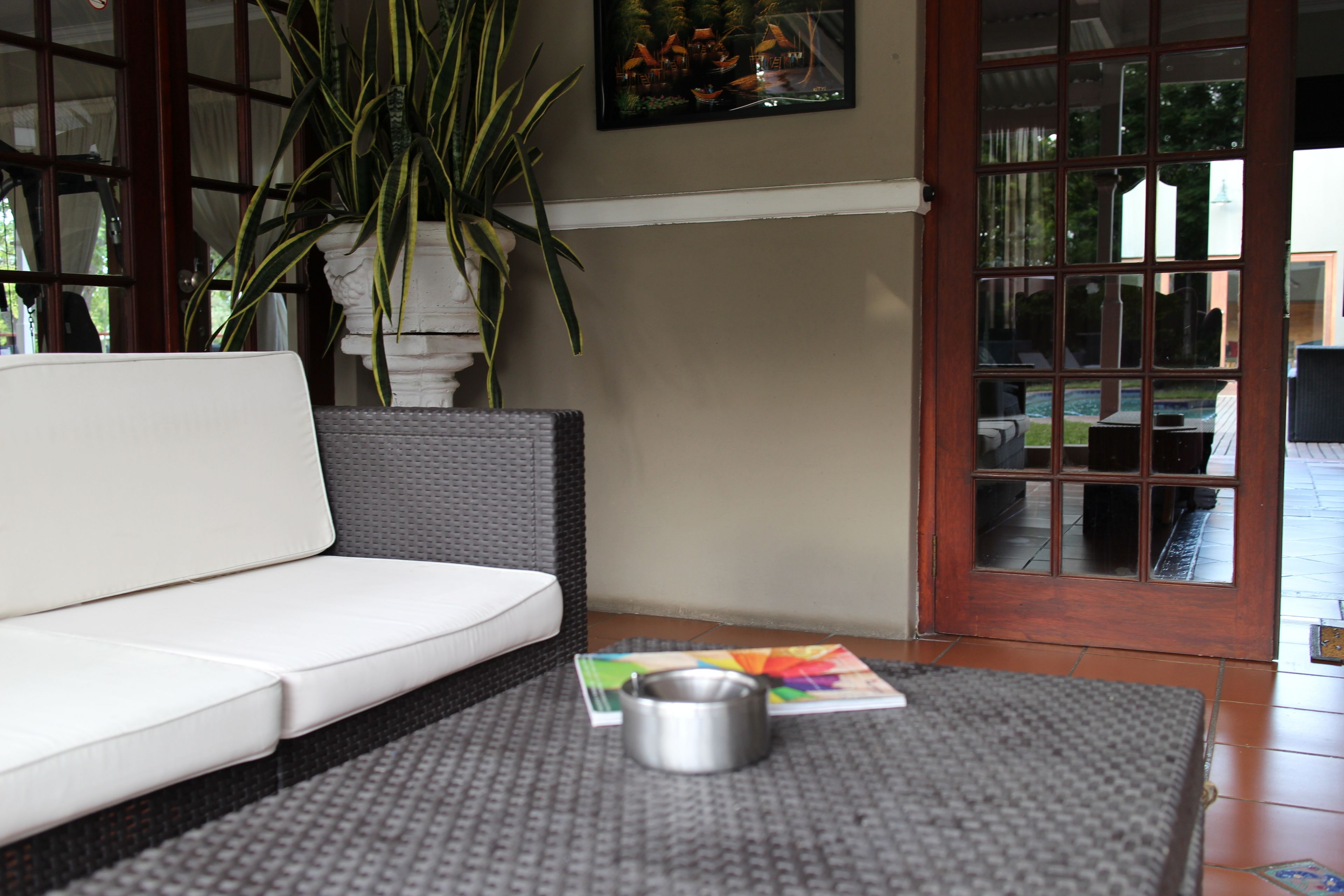 Ein Zimmer mit einem weißen Sofa, einem grauen Teppich, einem Metall-Aschenbecher und einer Topfpflanze.