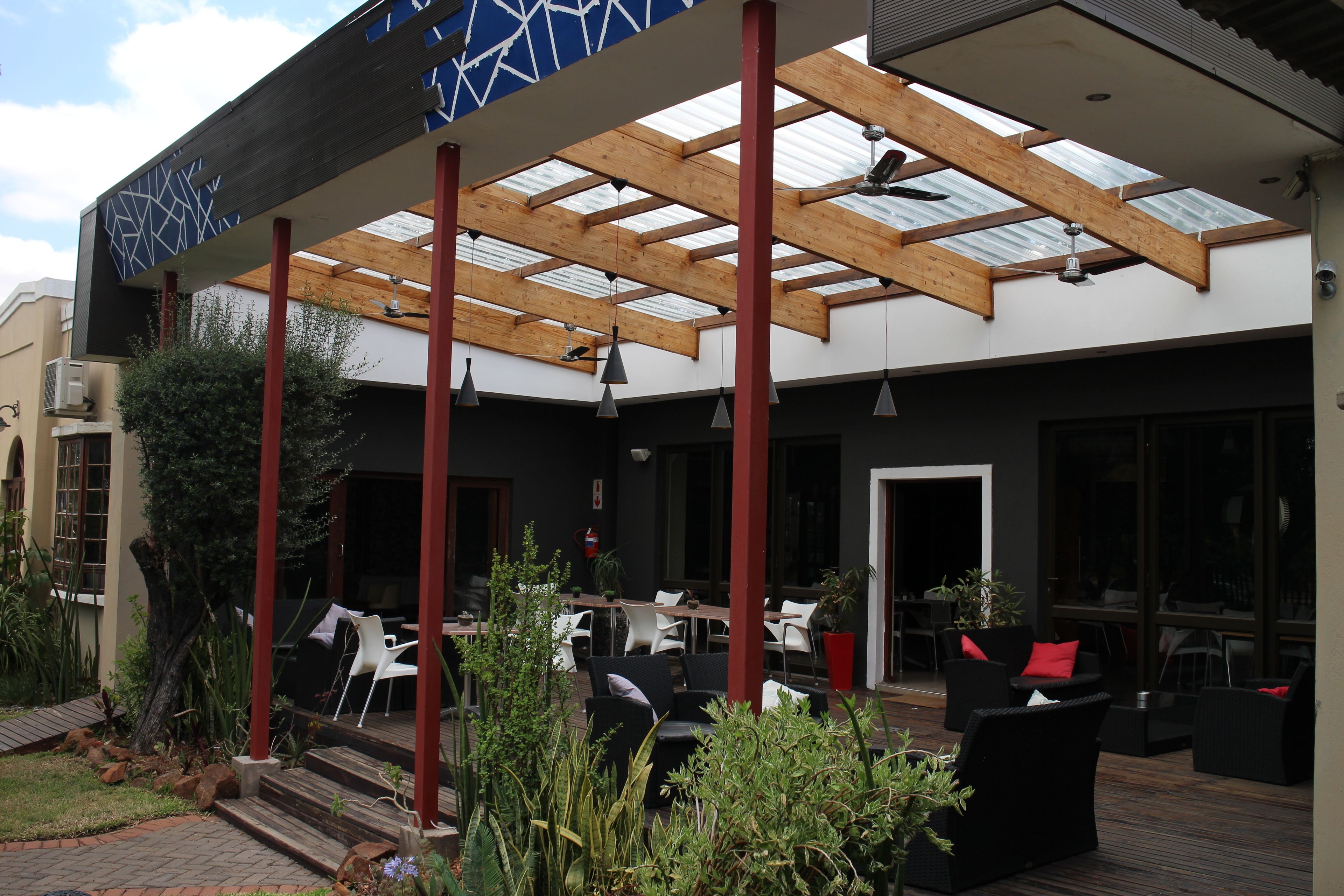 An outdoor patio with wooden beams, black and white furniture, and potted plants.