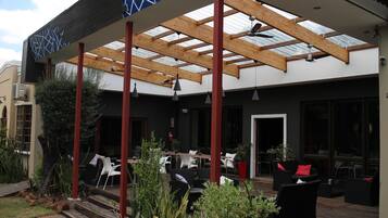 An outdoor patio with wooden beams, black and white furniture, and potted plants.