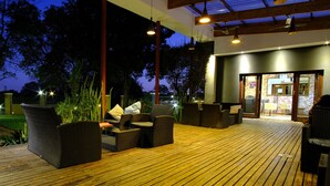 An outdoor deck with wicker furniture and a wooden floor, leading to a building with a glass door. - Cu Boutique Guest House (Phalaborwa)