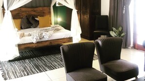 A bedroom with a canopy bed, a television, a dark wooden wardrobe, and two armchairs. - Cu Boutique Guest House (Phalaborwa)