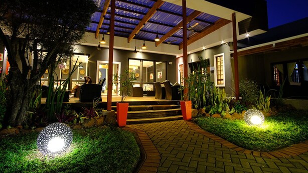 A modern house with a covered porch, outdoor seating, and a well-lit garden area at night. - Cu Boutique Guest House (Phalaborwa)