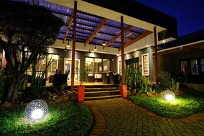 Una casa moderna con un porche cubierto, mobiliario de exterior y un jardín bien iluminado por la noche.