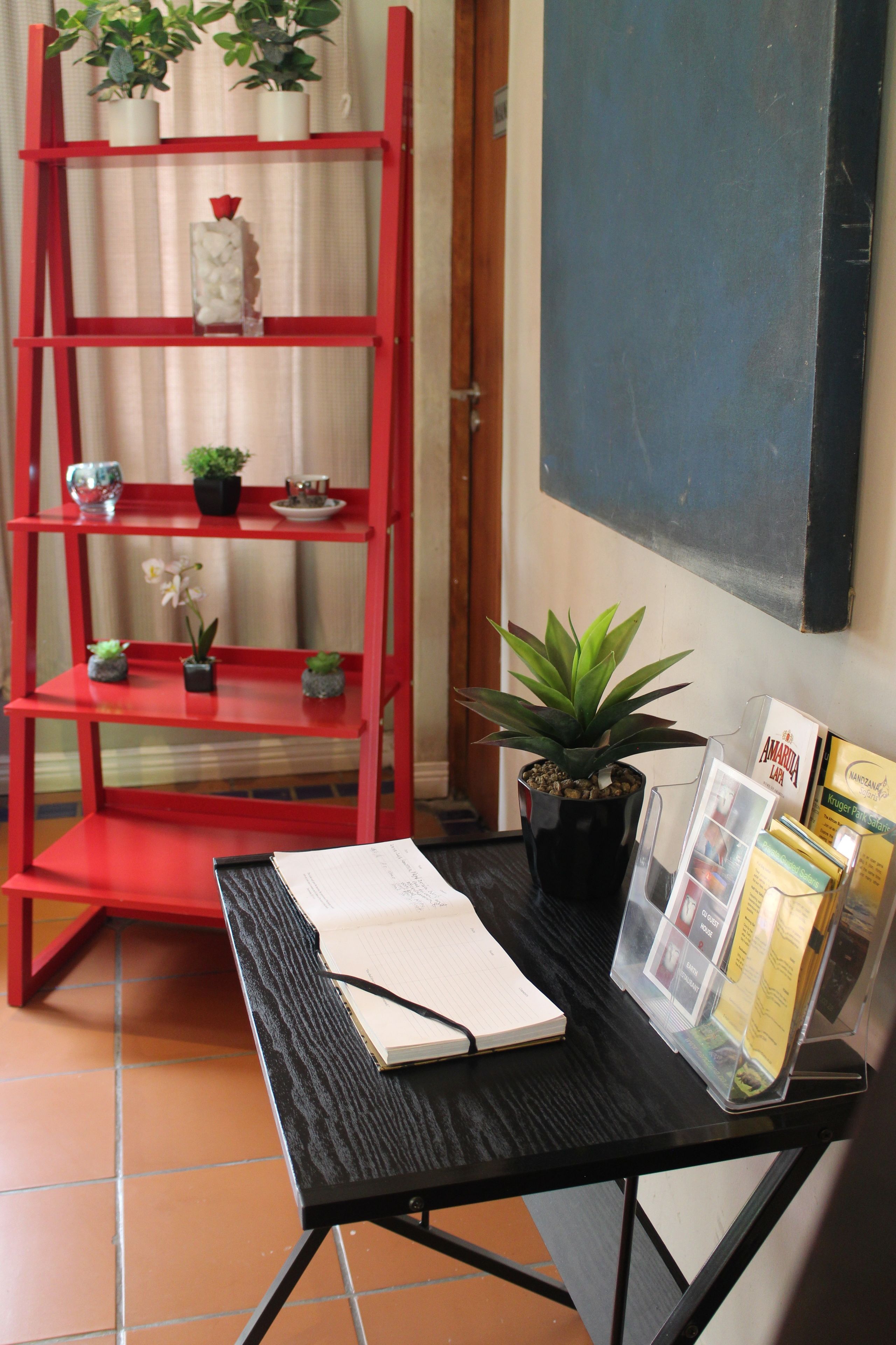 A red metal shelf with potted plants and a black table with a notebook and magazines.