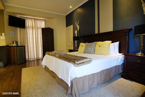 Habitación de hotel con una cama grande, un televisor de pantalla plana, un escritorio con lámpara y un ventanal con cortinas.