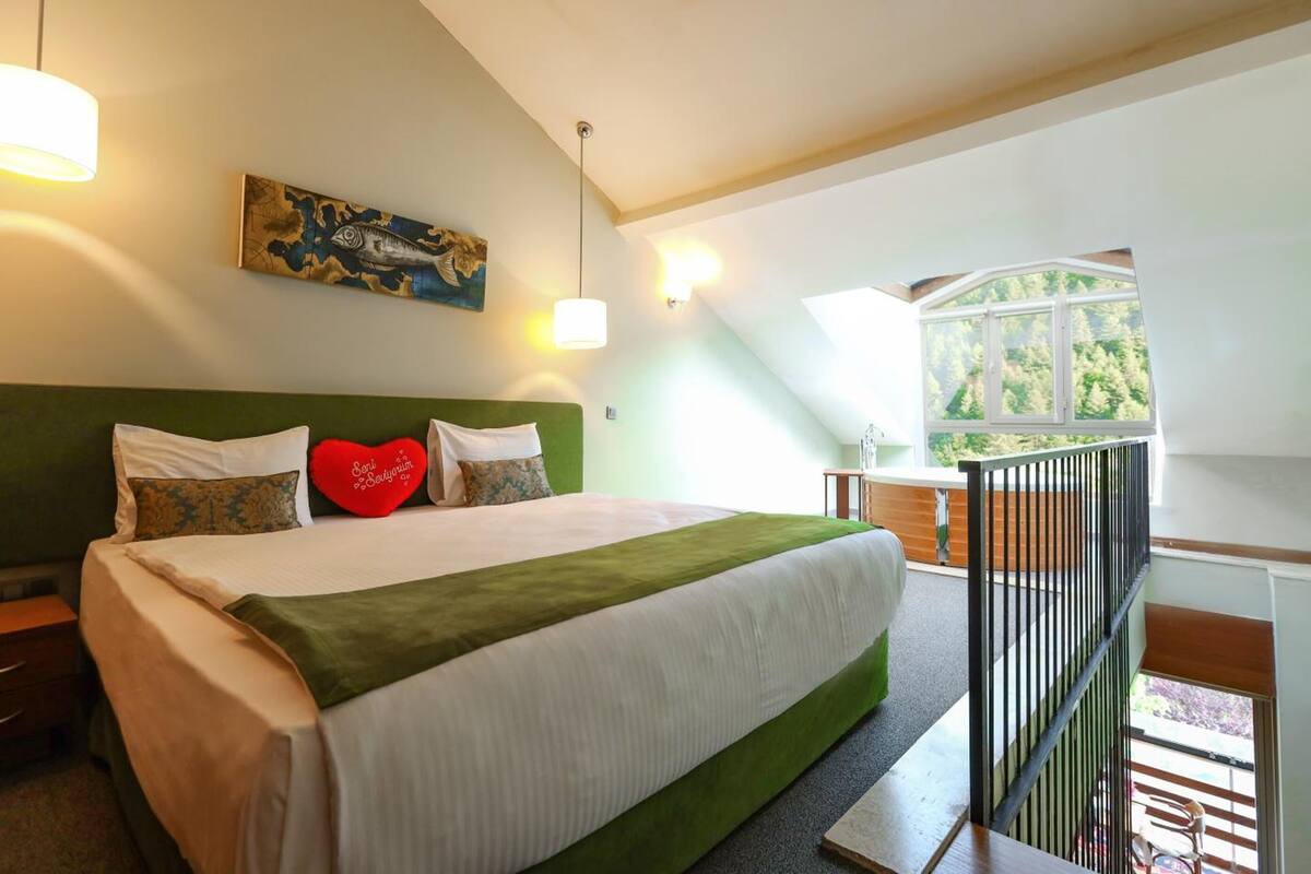 A bedroom with a large bed, a green headboard, a painting, and a window with a view of trees.