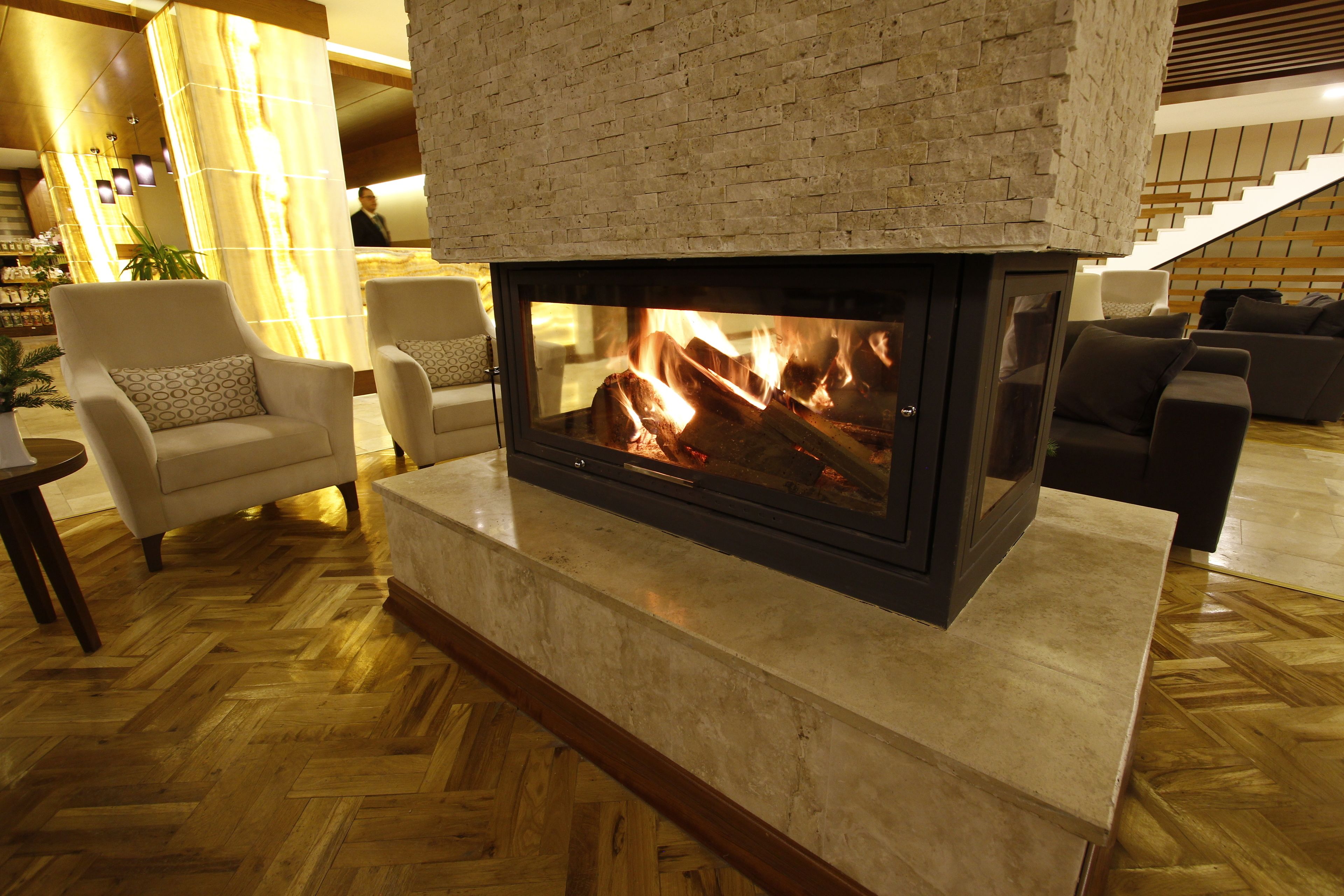 Una chimenea con revestimiento de ladrillo, un suelo de madera con patrón de espiga, y una zona de estar con sillones y sofá.