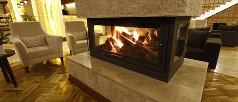 Una chimenea con revestimiento de ladrillo, un suelo de madera con patrón de espiga, y una zona de estar con sillones y sofá.