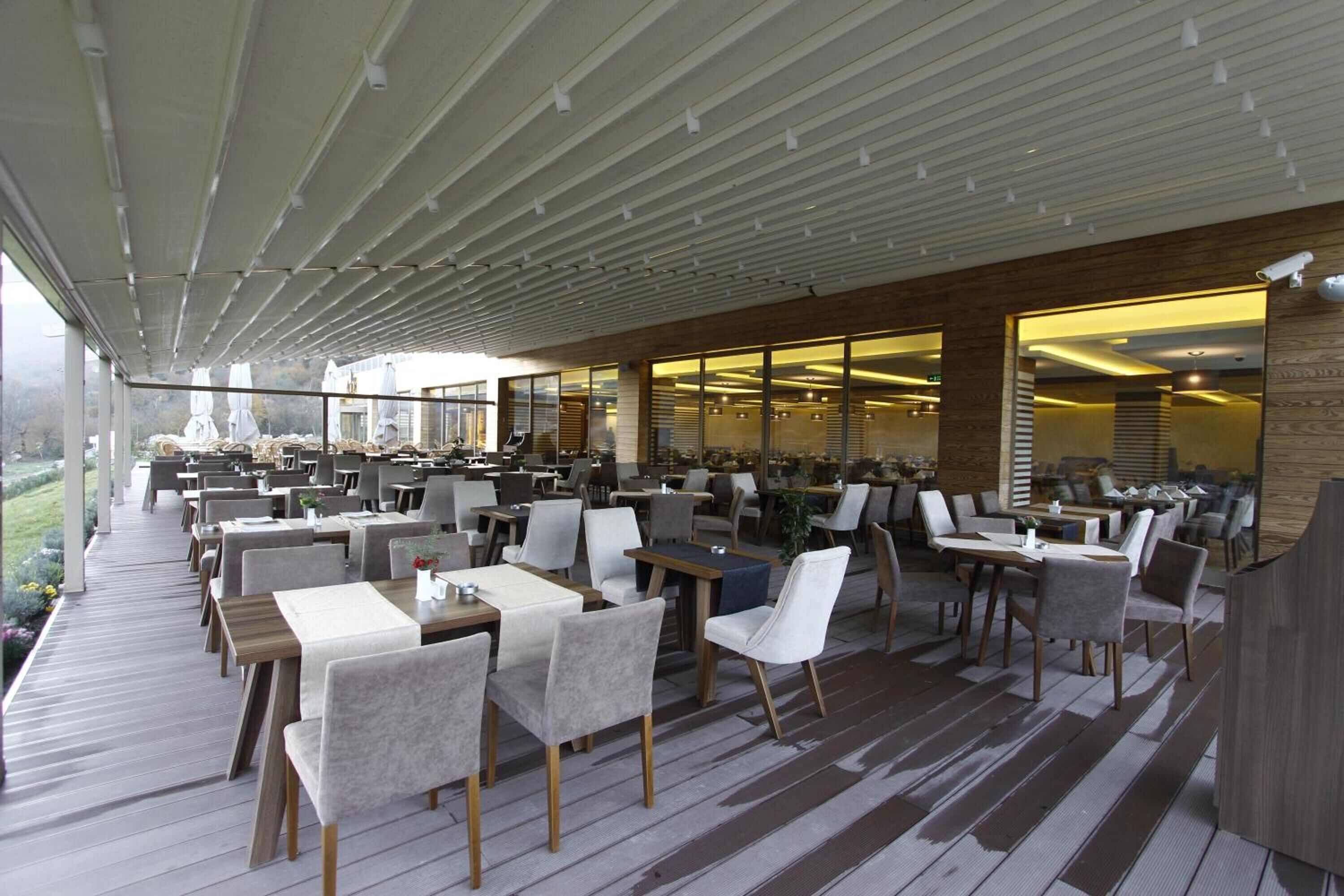 A spacious indoor dining area with multiple tables and chairs, large windows, and a wooden deck.
