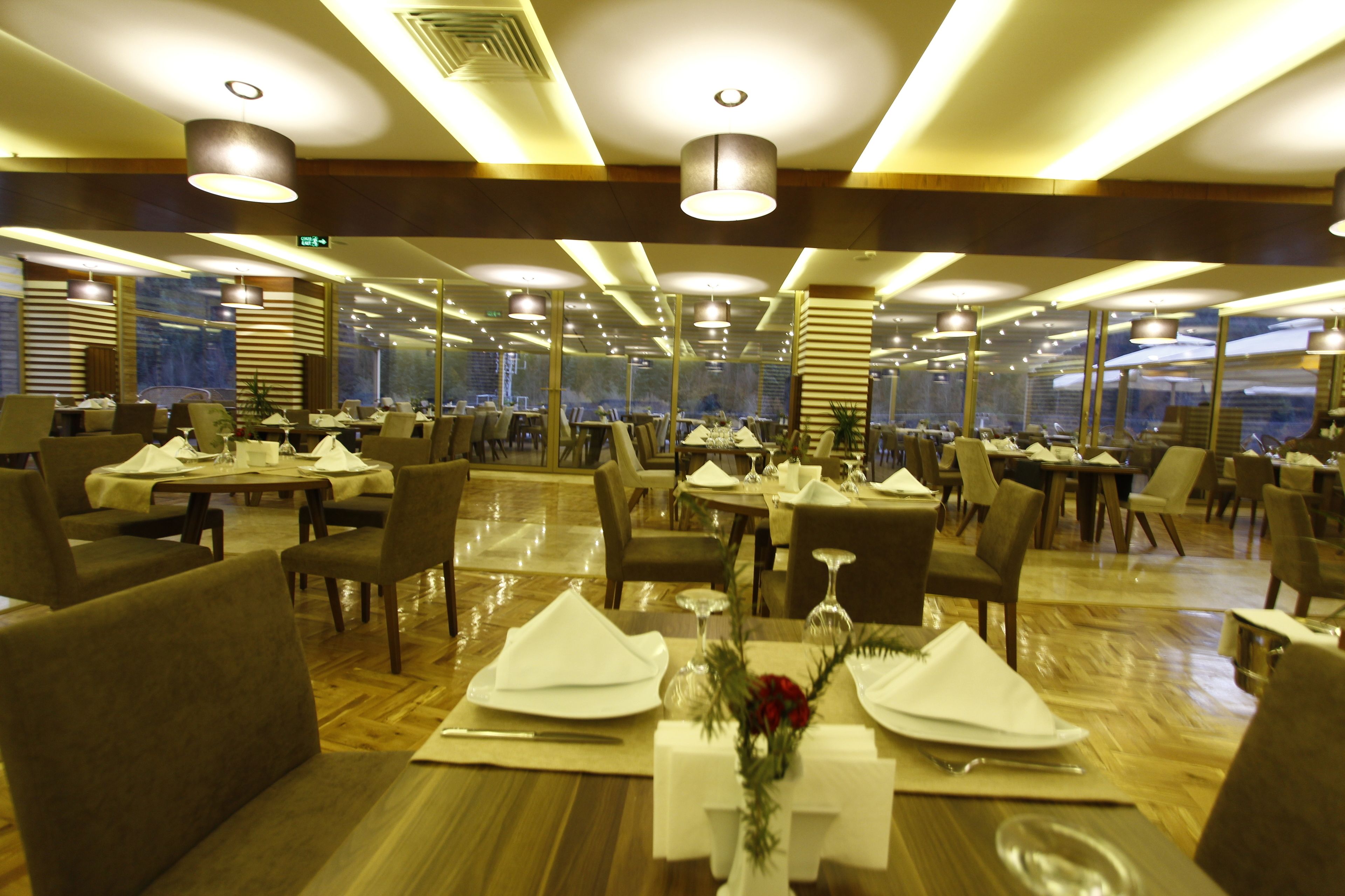 Un restaurante con varias mesas dispuestas para comer, con una decoración moderna, suelo de madera e iluminación contemporánea.