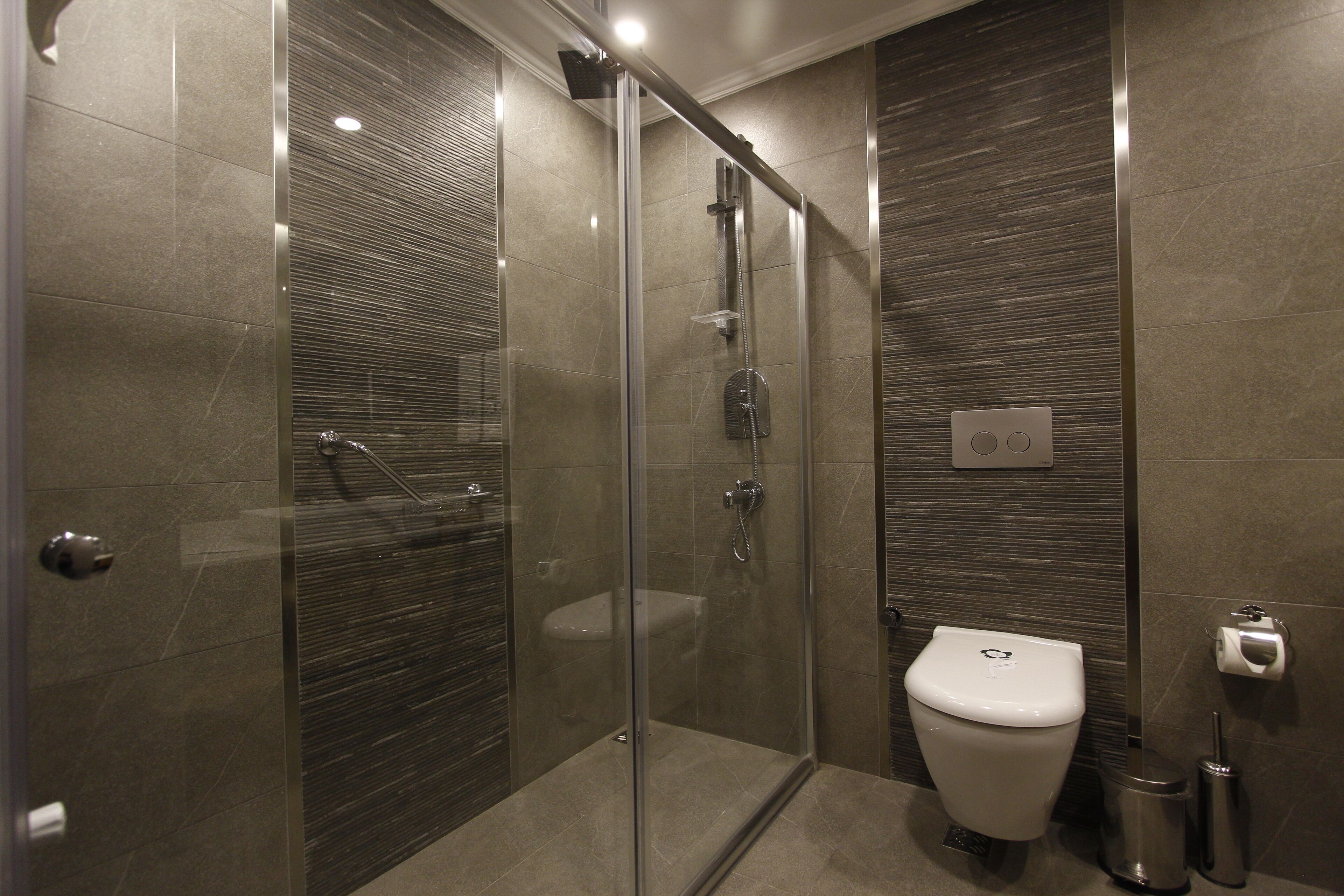 A modern bathroom with a glass-enclosed shower, a toilet, and a trash bin.