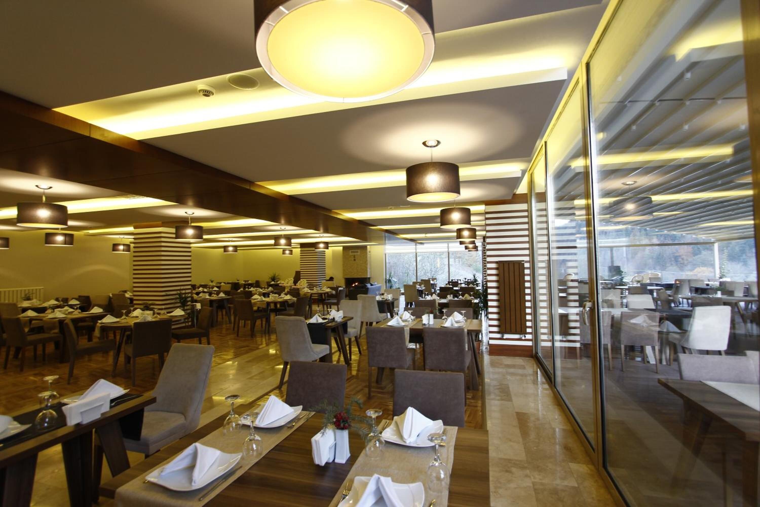 A spacious restaurant with multiple dining areas, modern lighting fixtures, and a view through large glass windows.