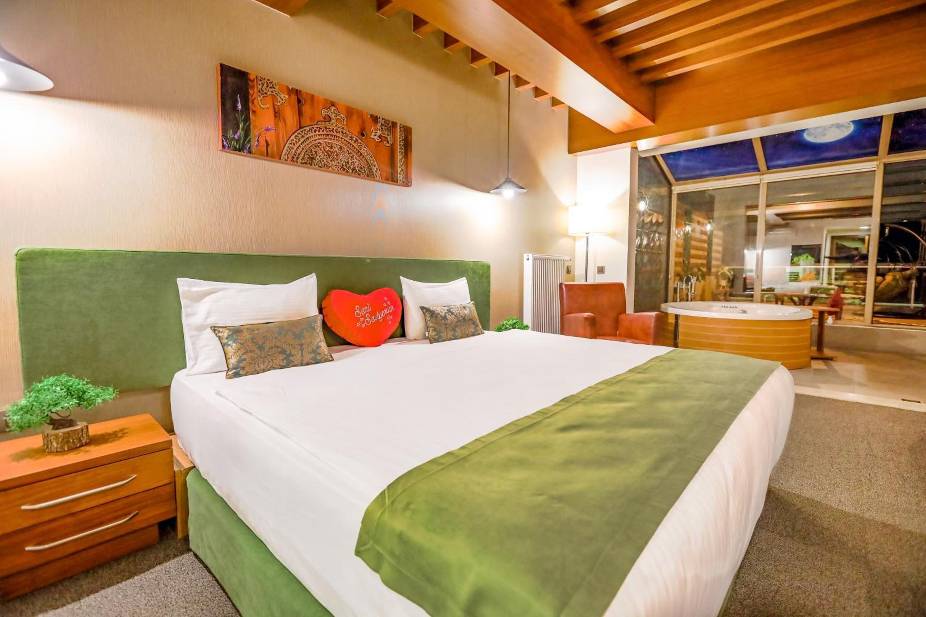 Ein modernes Hotelzimmer mit einem großen Bett, einem grünen Kopfteil und Blick auf den Außenbereich des Hotels.