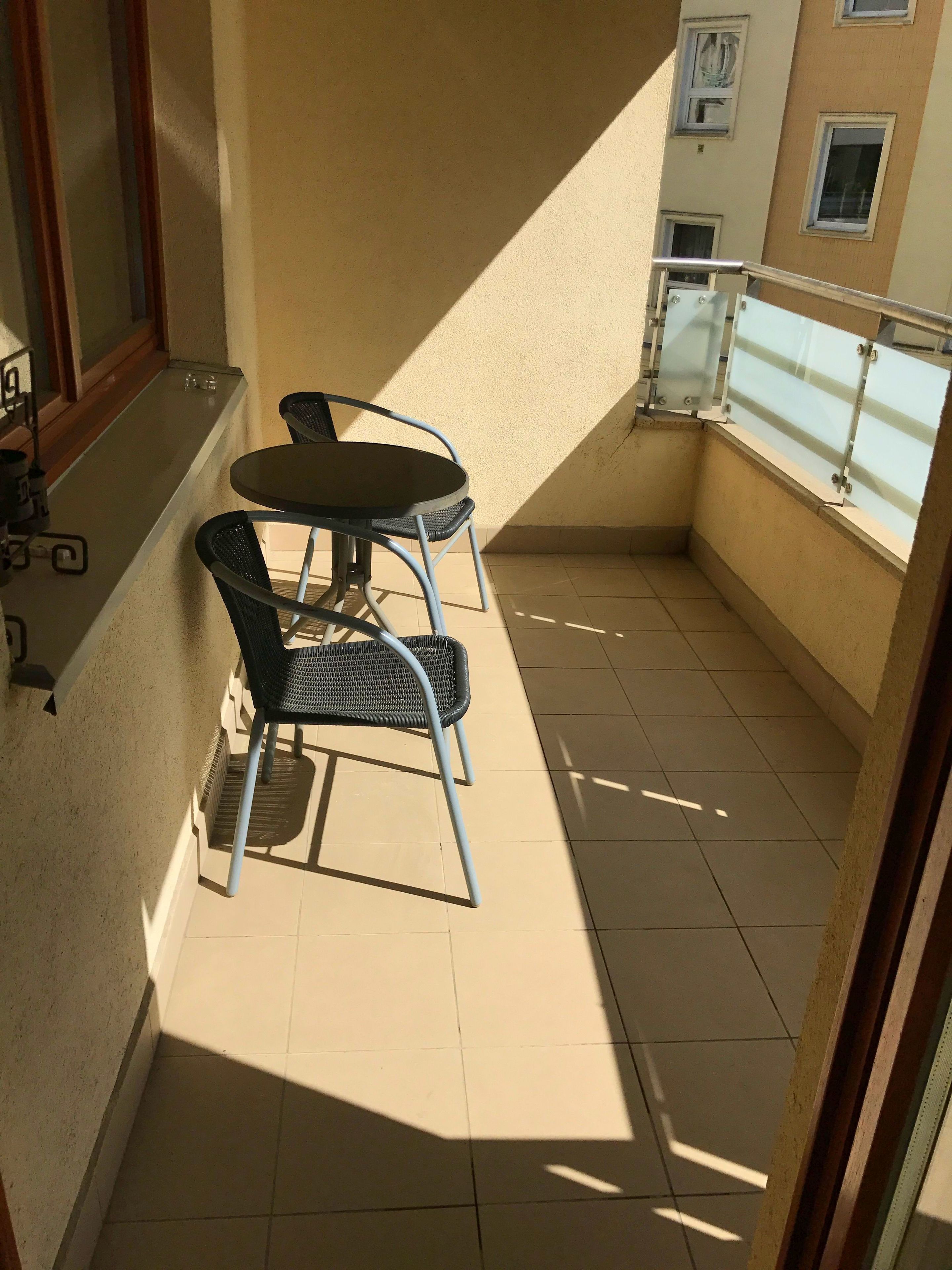 A small balcony with a table and two chairs, a window, and a tiled floor.
