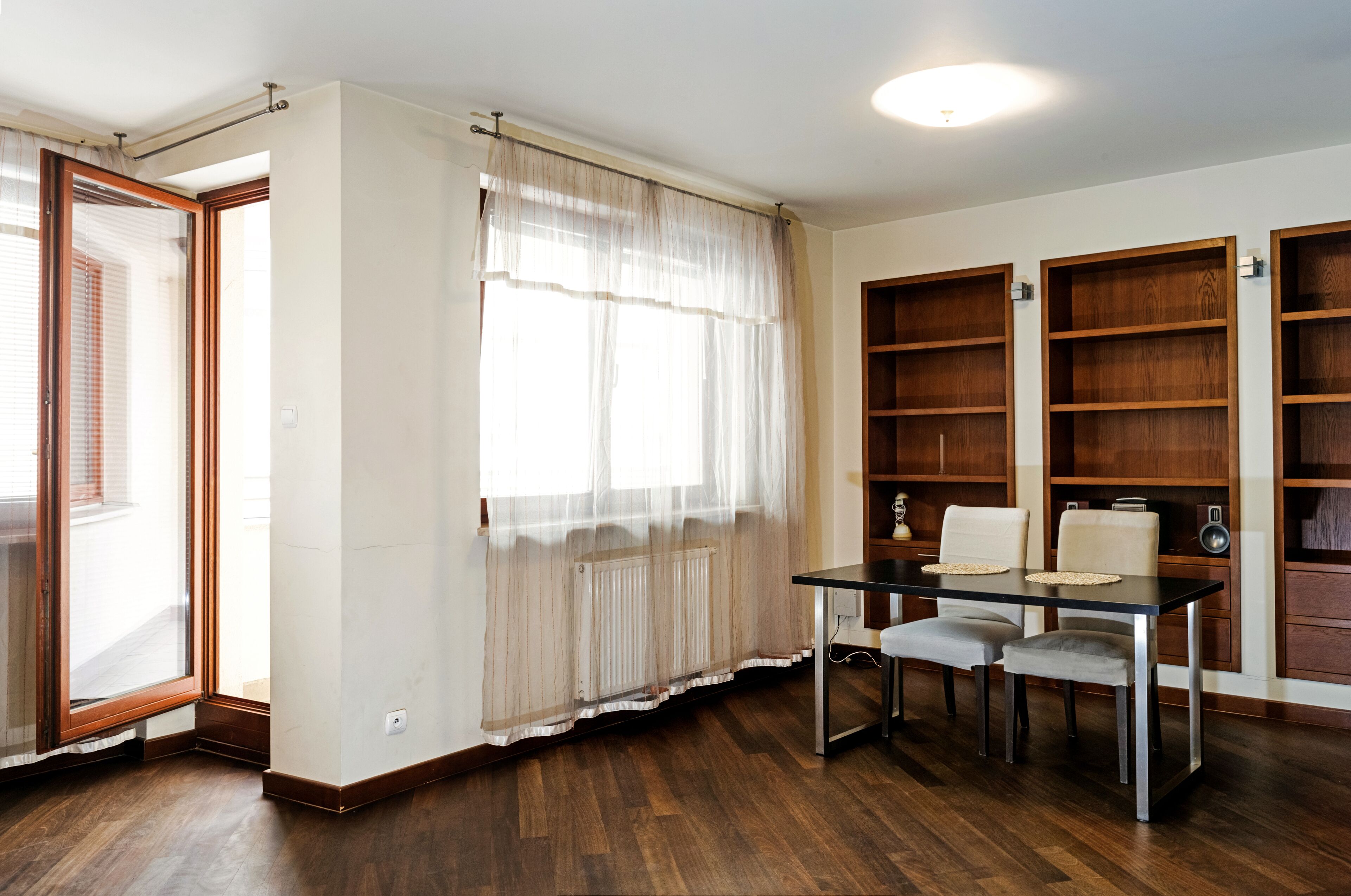 A room with a dining table, two chairs, a radiator, and wooden bookshelves.